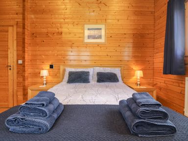 A bedroom with a double bed two bedside tables with lamps folded towels on the bed and wooden walls at Chywolow Lodge in Penzance