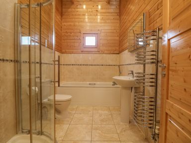 A bathroom with a shower, toilet, bathtub, sink, mirror, and towel radiator at Chywolow Lodge in Penzance