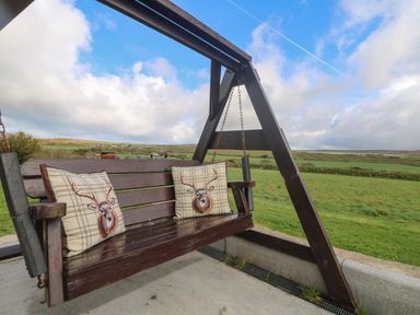 A wooden outdoor swing with deer print cushions overlooking green fields at Chywolow Lodge in Penzance