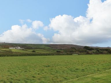 A grassy field with rolling hills and a house under a partly cloudy sky at Chywolow Lodge in Penzance