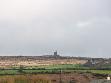 A rural landscape with fields houses and an old stone structure with a chimney at Chywolow Lodge in Penzance