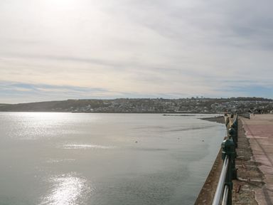 A waterfront promenade with railings and a view of a coastal town across the water at Chywolow Lodge in Penzance
