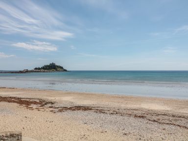A sandy beach with seaweed and pebbles with an island and castle in the distance at Chywolow Lodge in Penzance