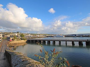 A harbor with a stone bridge over water and buildings along the shoreline at Chywolow Lodge in Penzance