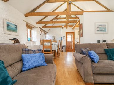 A living room with two sofas and blue pillows a dining table with chairs wooden beams on the ceiling and pictures on the walls at Mill in Nancegollan nr Porthleven