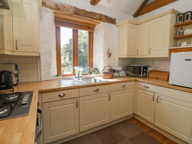 A kitchen with cream cabinets a wood countertop a gas stove a microwave a small refrigerator and a window at Mill in Nancegollan nr Porthleven