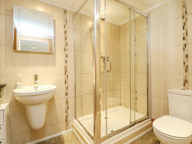 A bathroom with a wall-mounted sink a mirror a glass shower enclosure and a toilet at Mill in Nancegollan nr Porthleven