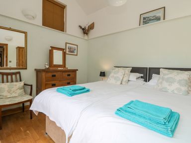 A bedroom with two beds with folded towels on each bed a wooden dresser a chair with cushions and framed pictures on the walls at Mill in Nancegollan nr Porthleven