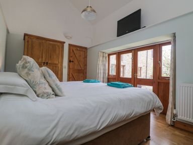 A bedroom with a double bed with pillows and folded towels wooden doors and a wall mounted television at Mill in Nancegollan nr Porthleven