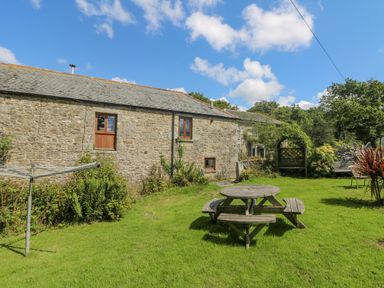 A stone house with wooden windows and a grass garden with a round wooden picnic table and a clothesline at Mill in Nancegollan nr Porthleven