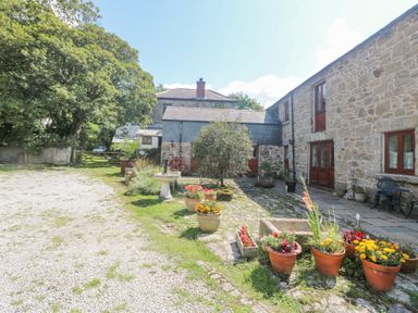 A gravel courtyard with potted plants and stone buildings with wooden doors at Mill in Nancegollan nr Porthleven