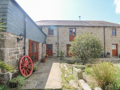 A stone courtyard with potted plants a red wagon wheel and multiple wooden doors at Mill in Nancegollan nr Porthleven