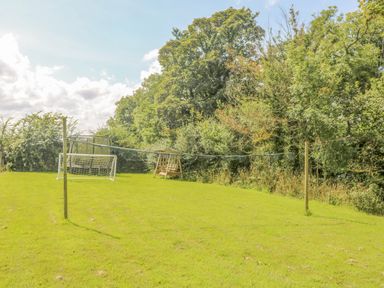 A grassy backyard with a soccer goal, a swing set, and two wooden poles with a net strung between them at Mill in Nancegollan nr Porthleven