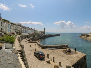 A coastal town with a row of houses along a curved waterfront and a stone pier extending into the sea at Mill in Nancegollan nr Porthleven