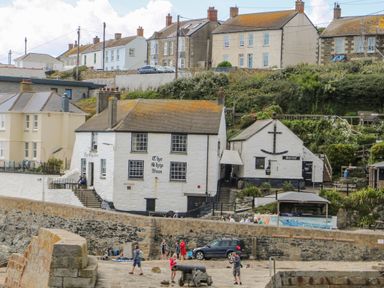 A waterfront with white buildings including The Ship Inn and people walking near a stone wall at Mill in Nancegollan nr Porthleven