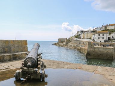 An old cannon on a stone platform overlooking a harbor with water and buildings at Mill in Nancegollan nr Porthleven