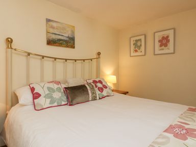 A bedroom with a bed with floral pillows and paintings on the wall and a lamp on a bedside table at Mill in Nancegollan nr Porthleven