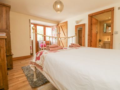 A bedroom with a metal bed frame wooden furniture towels on the bed a door leading to a bathroom and a window with curtains at Mill in Nancegollan nr Porthleven