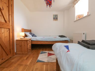 A bedroom with two single beds a wooden nightstand with a lamp a small rug and a closed wooden door at Mill in Nancegollan nr Porthleven