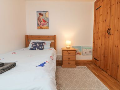 A bedroom with a single bed beside a wooden nightstand with lamp and a wardrobe with paintings on the walls at Mill in Nancegollan nr Porthleven