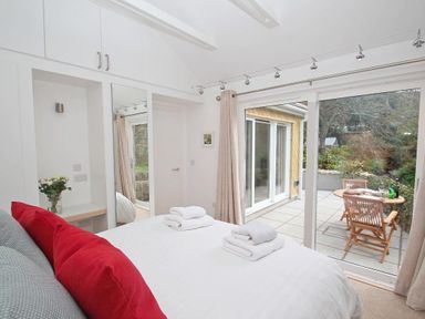 A bedroom with a bed and red pillows next to glass doors opening to a patio with a table and chairs at Cot Valley Cottage in St Just
