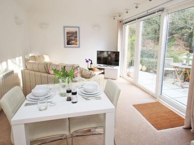 A dining table set for four near a sofa and a television in a living room with glass doors to a patio at Cot Valley Cottage in St Just