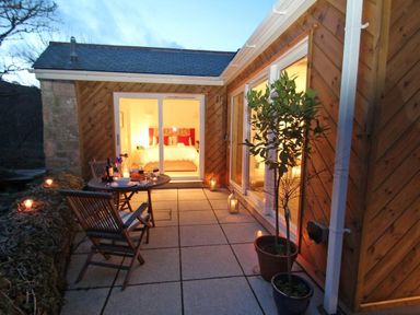 An outdoor patio with a table set for two and potted plants outside a wooden house at Cot Valley Cottage in St Just