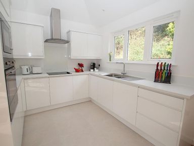 A kitchen with white cabinets, countertop appliances, a sink under windows, and a knife block at Cot Valley Cottage in St Just