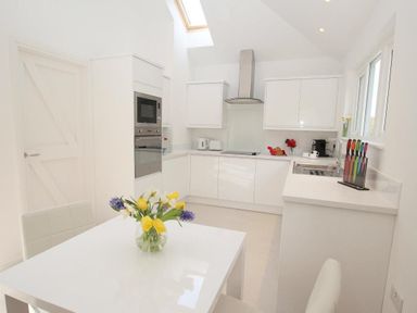 A kitchen with white cabinets a table with flowers and a skylight at Cot Valley Cottage in St Just