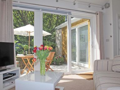 A living room with a vase of flowers on a table and a view of a patio with umbrellas at Cot Valley Cottage in St Just