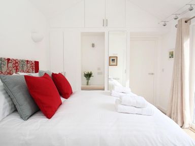 A bedroom with a bed with red and grey pillows and folded towels on top at Cot Valley Cottage in St Just