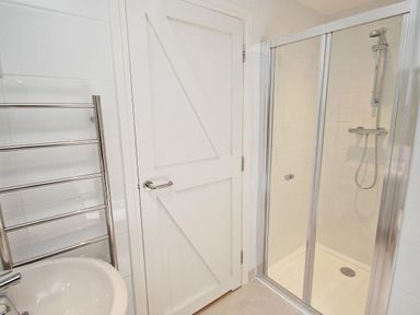 A bathroom with a glass-enclosed shower a white door a towel rack and a sink at Cot Valley Cottage in St Just