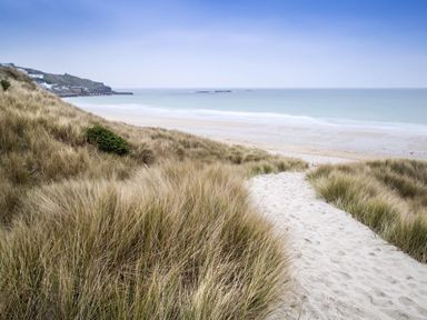 A sandy path through tall grass leading to a beach with the ocean and distant coastline visible at Cot Valley Cottage in St Just