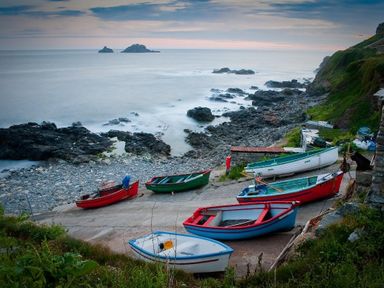 Boats on a rocky shore near the sea with a cliffside and small islands in the distance at Cot Valley Cottage in St Just