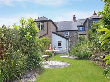 A garden with green plants and a small round table with two chairs in front of a stone and stucco house at Pippin in Lelant