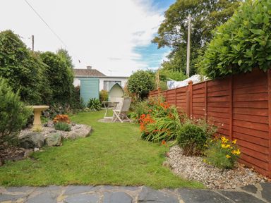 A garden with green lawn flowers wooden table and chairs a birdbath and a red wooden fence at Pippin in Lelant