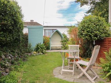 A garden with grass a small round wooden table with two chairs a wooden shed a bench with a canopy and plants at Pippin in Lelant