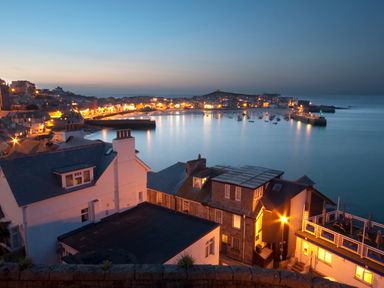 A coastal town at dusk with houses near a harbor filled with boats and illuminated streets at Pippin in Lelant