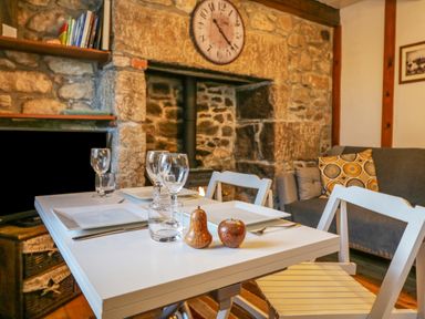 A dining table with glassware and plates near a stone wall fireplace in a room with a sofa and cushions at Pippin in Lelant