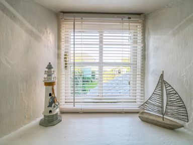 A small window with white blinds and nautical decorations including a lighthouse and a sailboat model at Pippin in Lelant