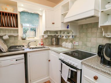 A kitchen with a dishwasher sink stove kettle and shelves with cups and plates at Pippin in Lelant