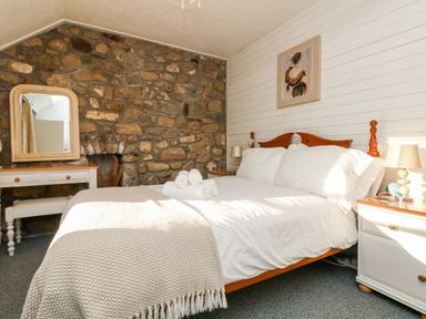 A bedroom with a double bed pillows bedside tables lamps a dresser mirror and a stone wall at Pippin in Lelant