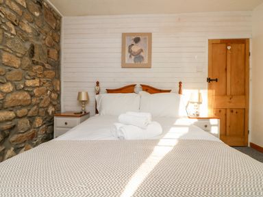 A bedroom with a double bed white bedding two bedside tables with lamps a stone wall and a wooden door at Pippin in Lelant