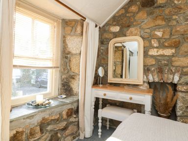 A stone wall bedroom corner with a window, curtains, a vanity table with mirror and stool at Pippin in Lelant