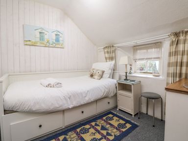 A small bedroom with a single bed bedside table stool and a window at Pippin in Lelant