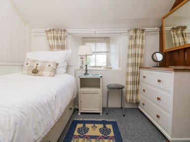 A bedroom with a single bed side table lamp stool and chest of drawers at Pippin in Lelant