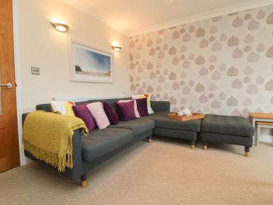 A living room with a grey corner sofa with cushions and a yellow throw and a tray with teapot and cups on the sofa at Ocean Blue in Porthtowan