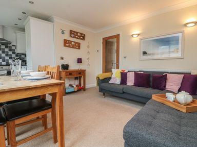 A living room with a dining table and chairs next to a kitchen area with a sofa and cushions at Ocean Blue in Porthtowan