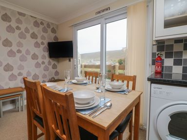 A dining area with a wooden table set for four with plates and glasses next to sliding glass doors and a washing machine at Ocean Blue in Porthtowan