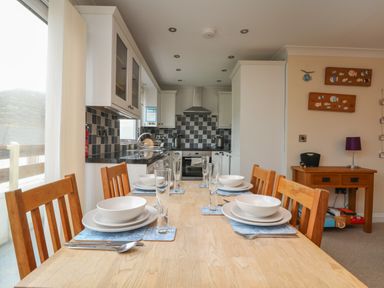 A dining table set with plates bowls glasses and cutlery in a kitchen with checkered backsplash and wooden chairs at Ocean Blue in Porthtowan